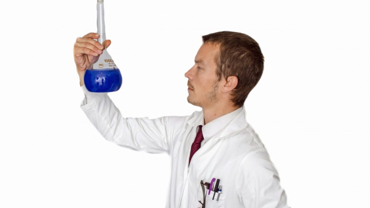 man in lab coat examining beaker with blue liquid